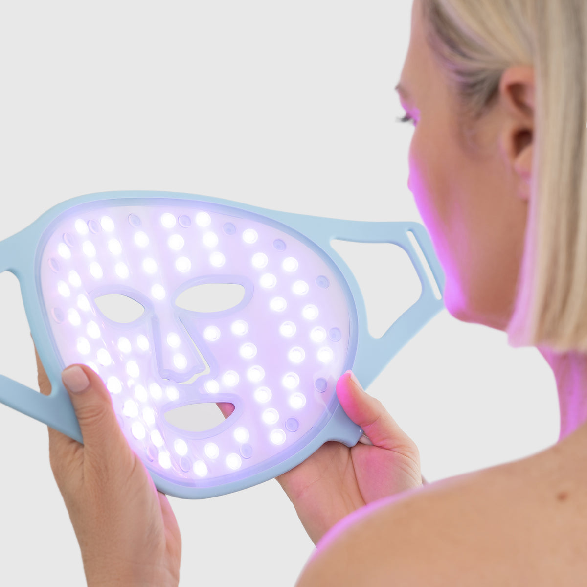 Woman holding LED light therapy face mask used for acne treatment and skin rejuvenation.