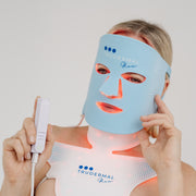Person wearing a blue LED face mask with visible branding on a plain background