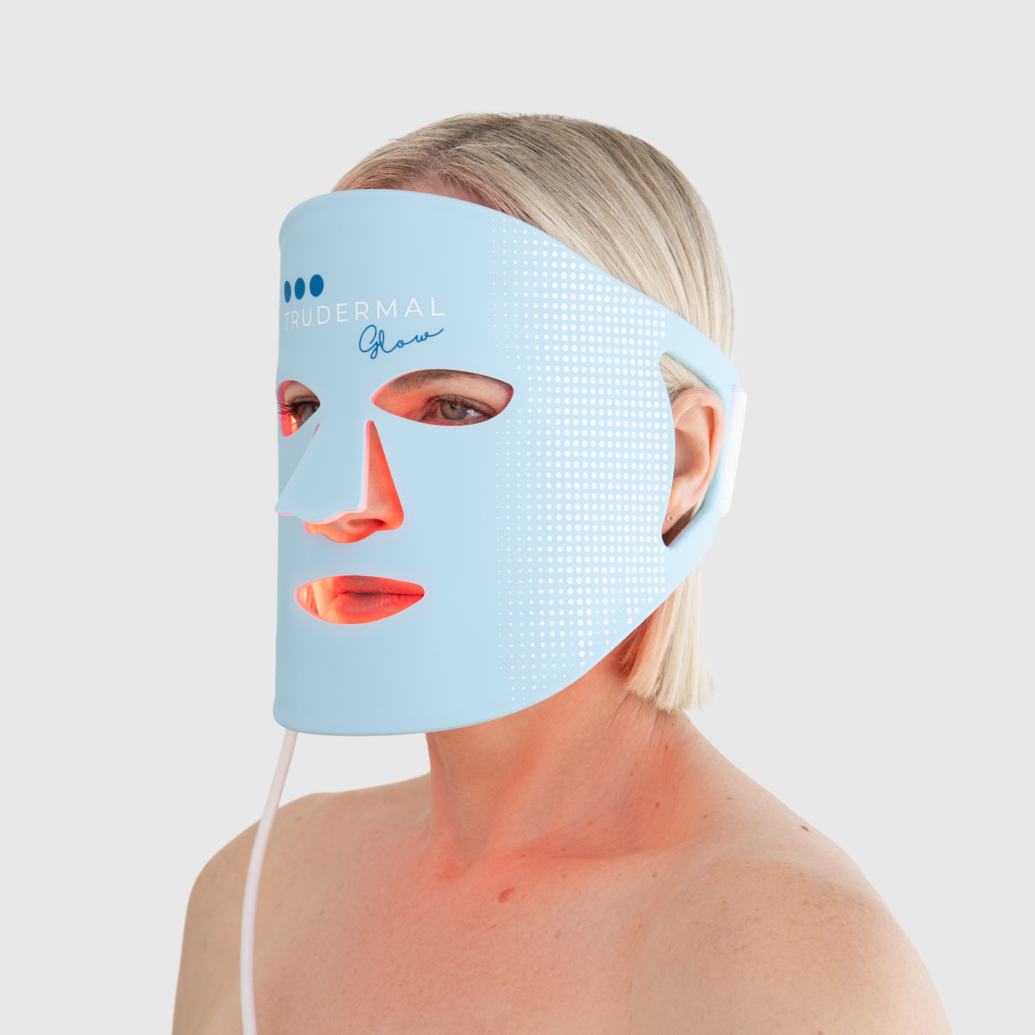 Woman using the Trudermal Glow LED light therapy face mask for at-home skin rejuvenation treatment.