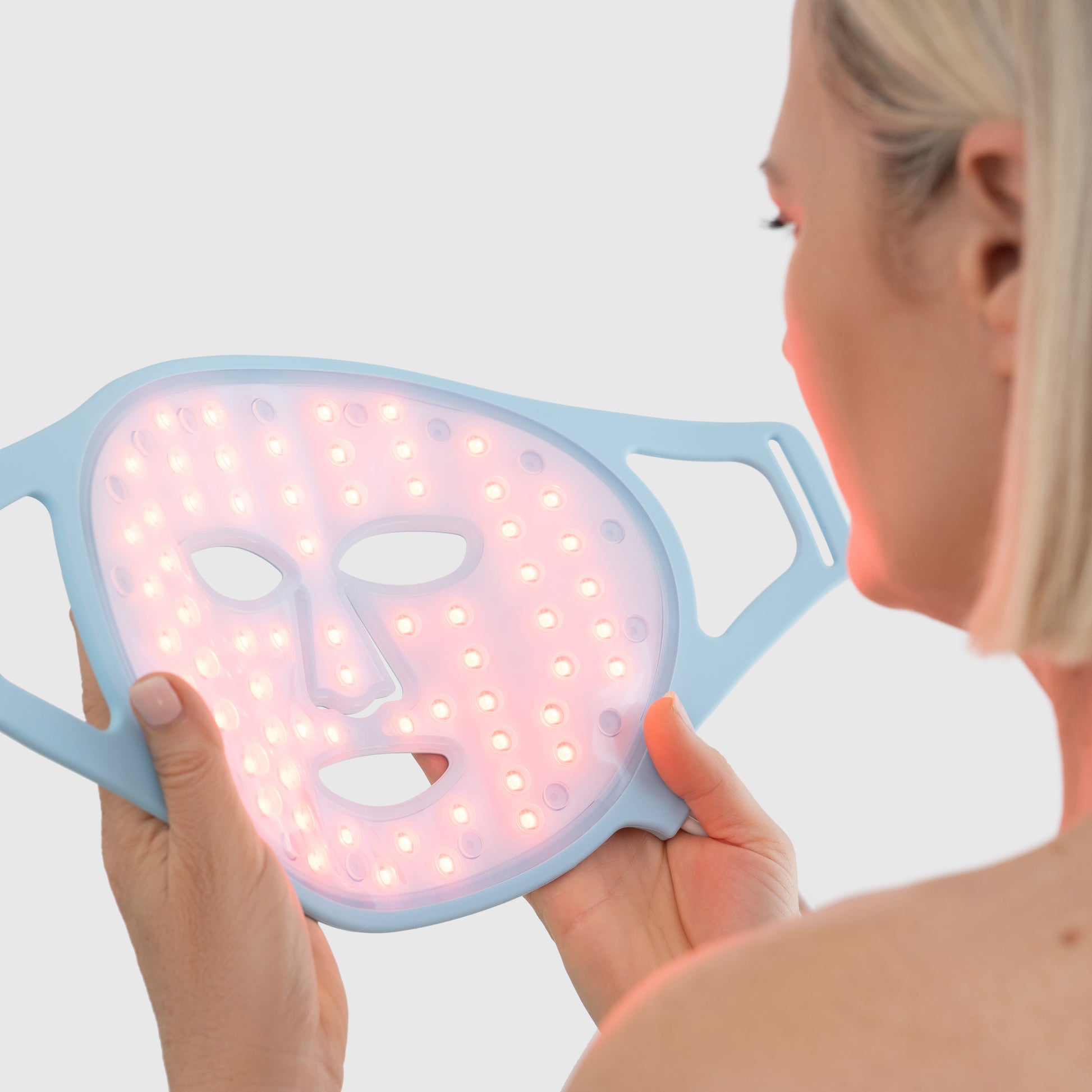 Woman holding red light therapy face mask designed to boost collagen and reduce fine lines.