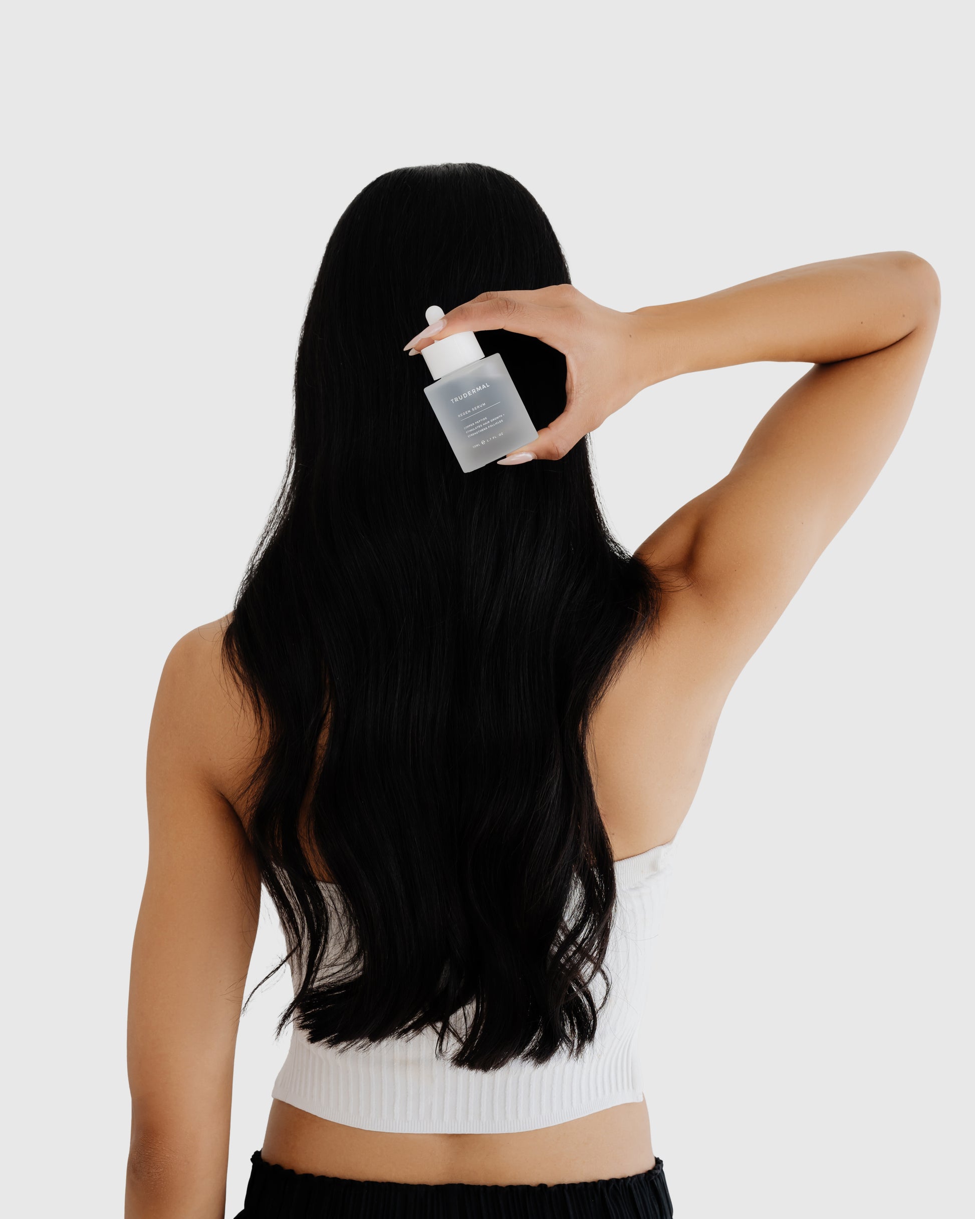 Woman holding hair growth serum designed to nourish the scalp and support healthy hair growth.