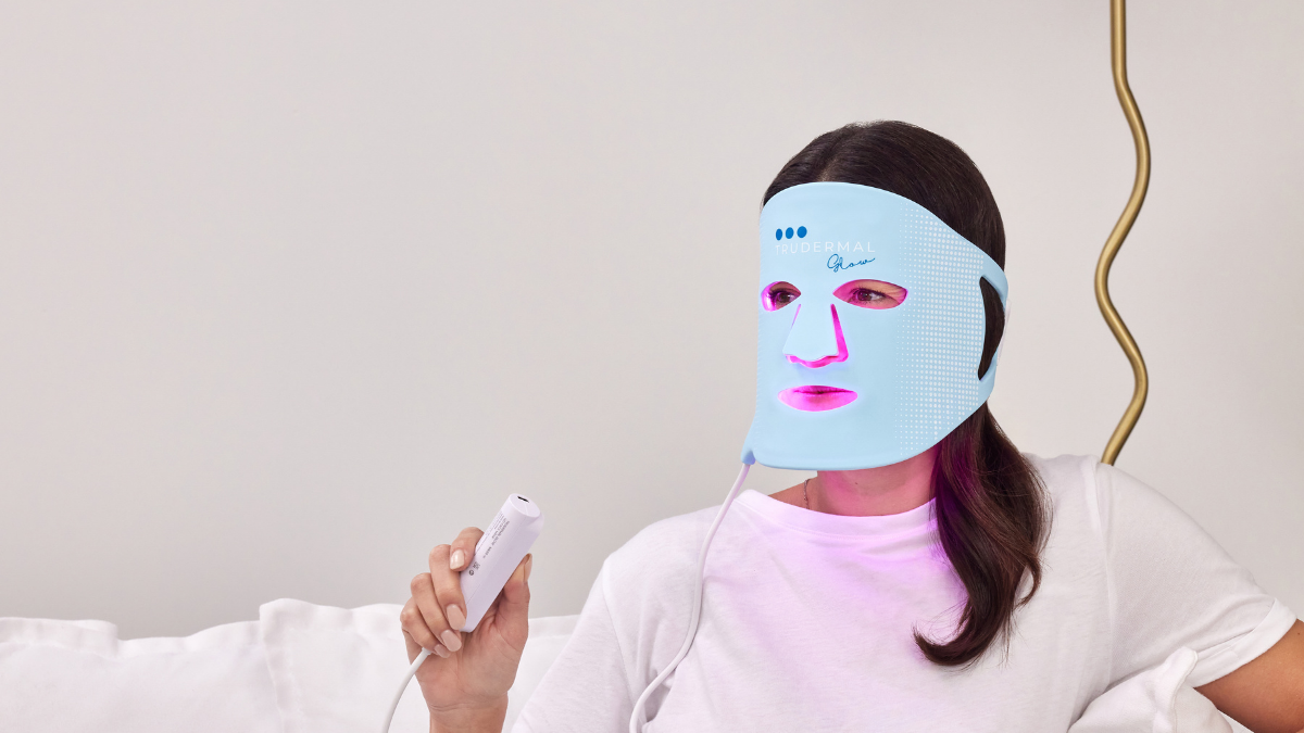 Woman wearing Trudermal LED light therapy face mask for acne treatment and skin rejuvenation.